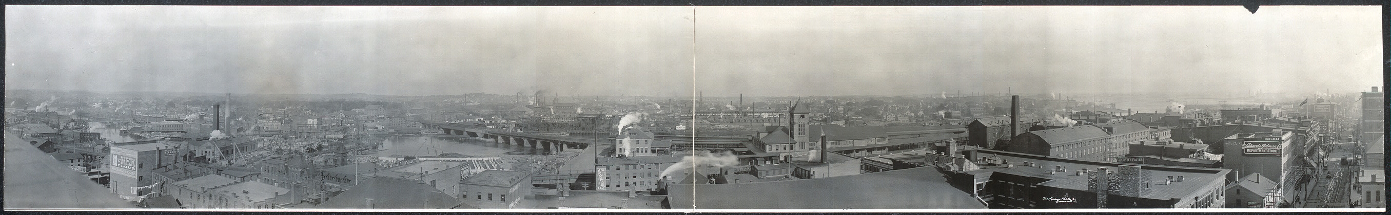A 1909 panorama of Bridgeport with factory roofs, chimneys, waterways and a railway bridge.