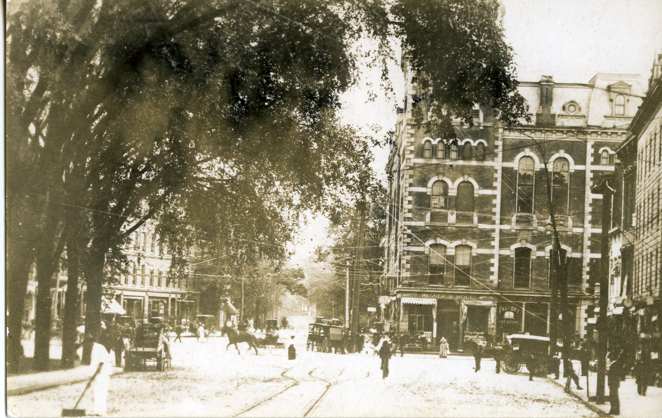 Looking south through Stamford’s Atlantic Square, with horse-drawn vehicles, pedestrians, shops and tracks beneath street trees